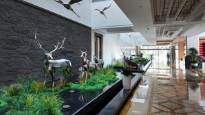 Eine moderne Lobby mit schwarzer Steinwand, spiegelndem Boden und einer langen Rezeption mit Pflanzen.
