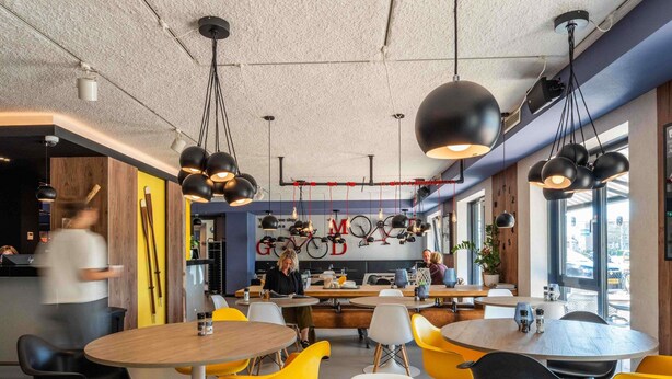 Un intérieur de restaurant moderne avec des tables rondes, des chaises jaunes et noires, et des luminaires suspendus.