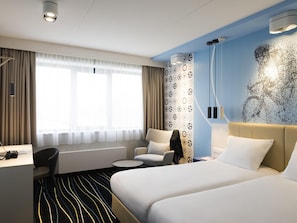 Habitación de hotel con cama, escritorio, silla, mesa redonda y pared con diseño decorativo.