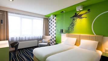 A hotel room with a bed, a chair, a desk, and a window with curtains.