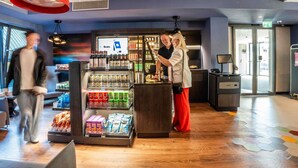 Un hall d’hôtel moderne doté d’un kiosque en libre-service, d’un bar et d’un plancher en bois recouvert de carreaux hexagonaux.