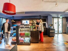 Un vestíbulo de hotel moderno con un quiosco de autoservicio, una zona de bar y un suelo de madera con baldosas hexagonales.
