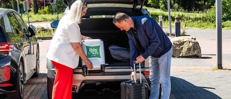 A car with its trunk open, luggage in the back, and a person handling a suitcase.