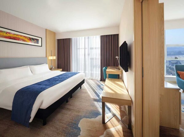 A hotel room with a large bed, a desk, a TV, and a view of the city. - ibis Styles Changsha International Exhibition Center (Changsha)