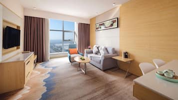 Una habitación de hotel moderna con un ventanal grande, un sofá, una mesa de comedor y un televisor.