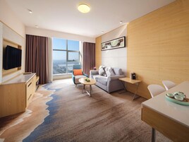Una habitación de hotel moderna con un ventanal grande, un sofá, una mesa de comedor y un televisor.