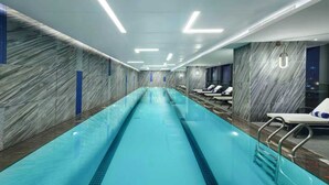 An indoor swimming pool with a long, narrow design, surrounded by marble walls and equipped with lounge chairs and a glass barrier. - ibis Styles Changsha International Exhibition Center (Changsha)