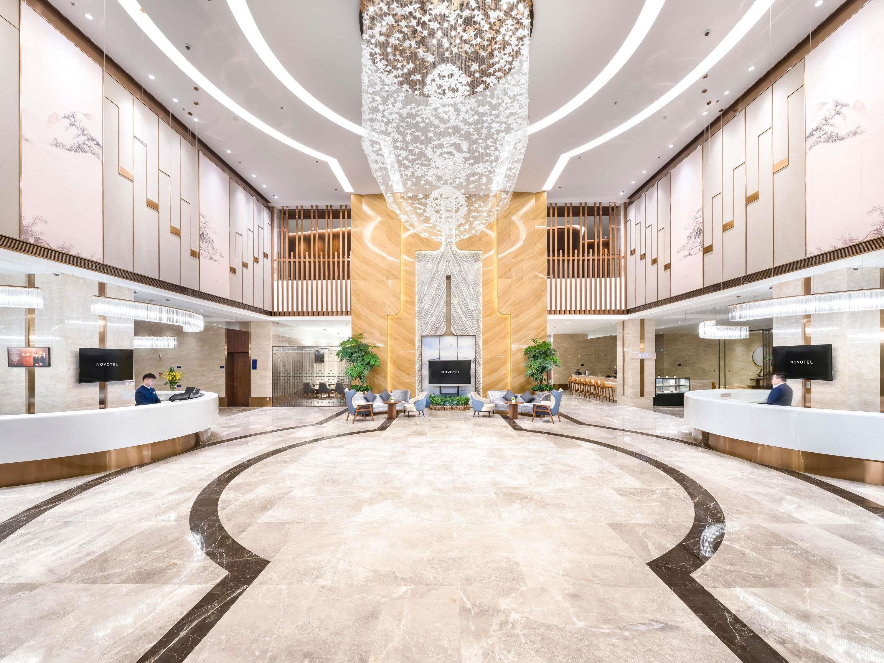 A hotel lobby with a reception desk, seating area, and a large chandelier.