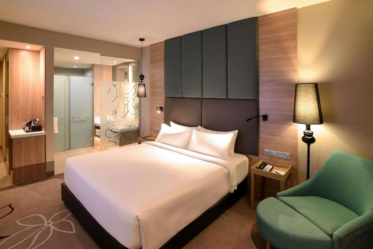 Una camera d'albergo con un letto grande, comodini, una poltrona verde e uno specchio.