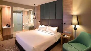 A hotel room with a large bed, bedside tables, a green armchair, and a mirror.
