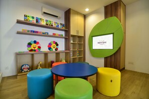 A children's play area with colorful stools, a round table, alphabet blocks, and a cartoon character.