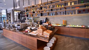 Una barra de desayuno moderna con diversas opciones de alimentos, una máquina de café y una exhibición de jarrones decorativos.
