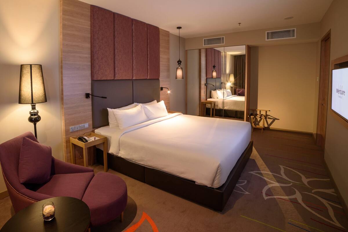 Una camera d'albergo con un letto grande, una sedia, una scrivania e uno specchio.