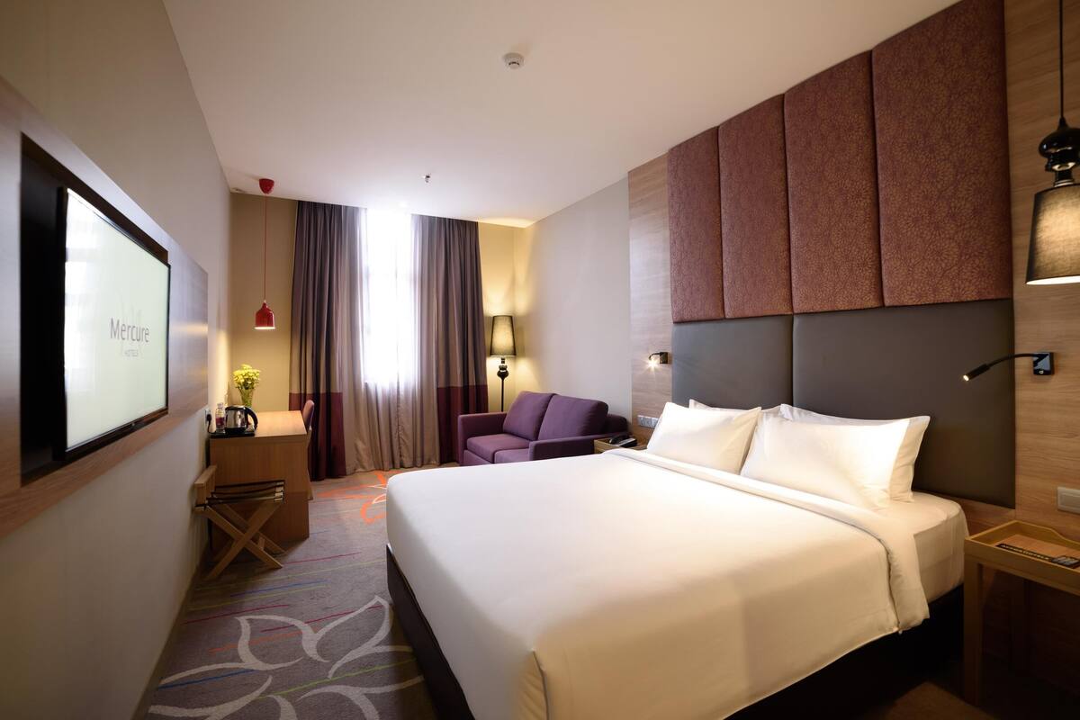 Camera d'hotel con un letto grande, una scrivania, una sedia e un televisore che mostra "Mercure HOTEL".