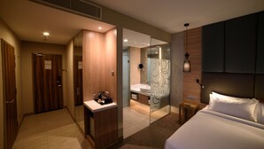 Una habitación de hotel moderna con una cama, una mesita de noche, un espejo, un baño con lavabo y ducha, y un armario de madera.