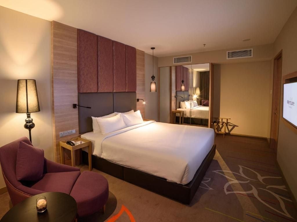 Habitación de hotel con cama, una silla, una mesita, una lámpara y un espejo.