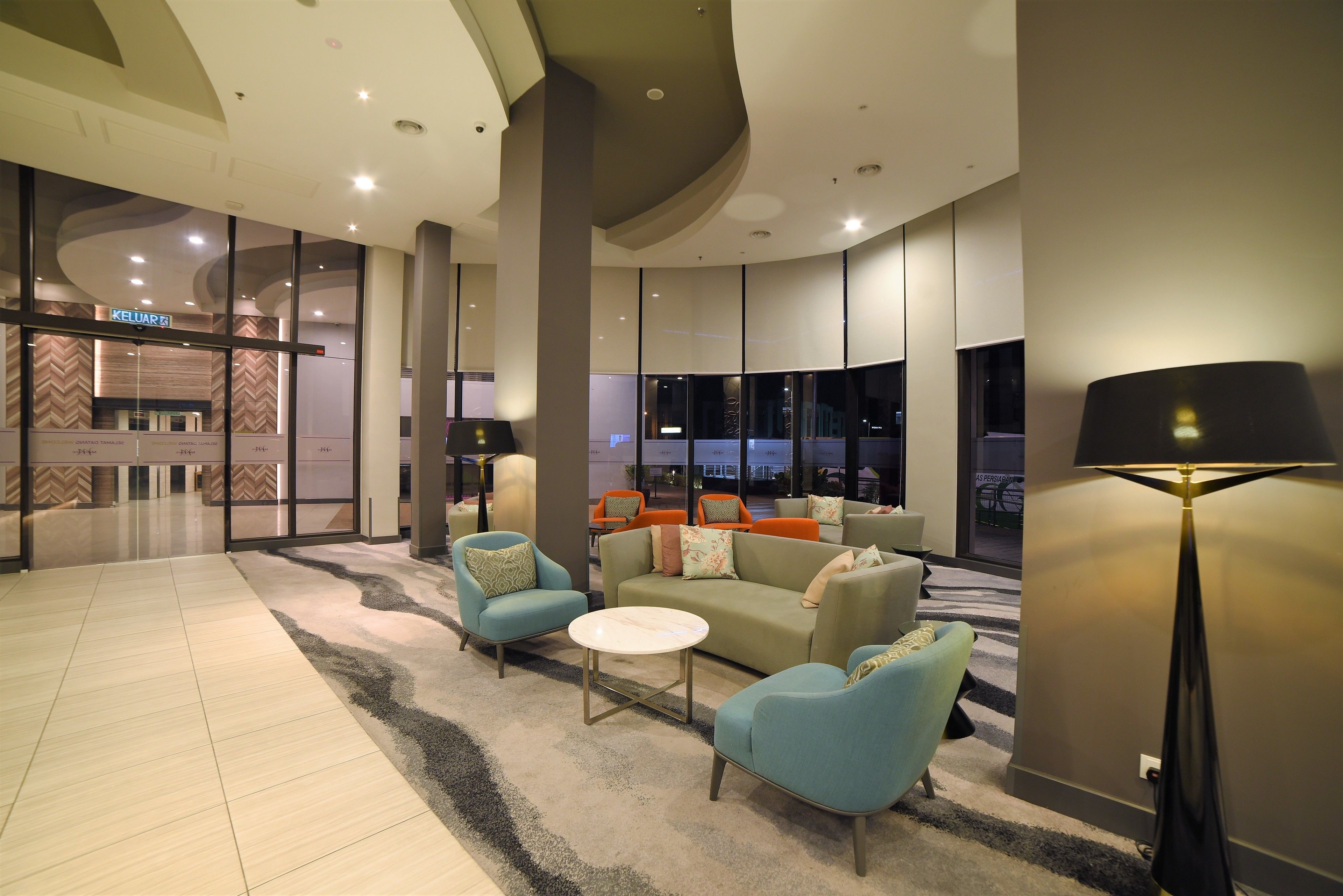 A modern lobby with a seating area, a KELUAR sign, and large windows.