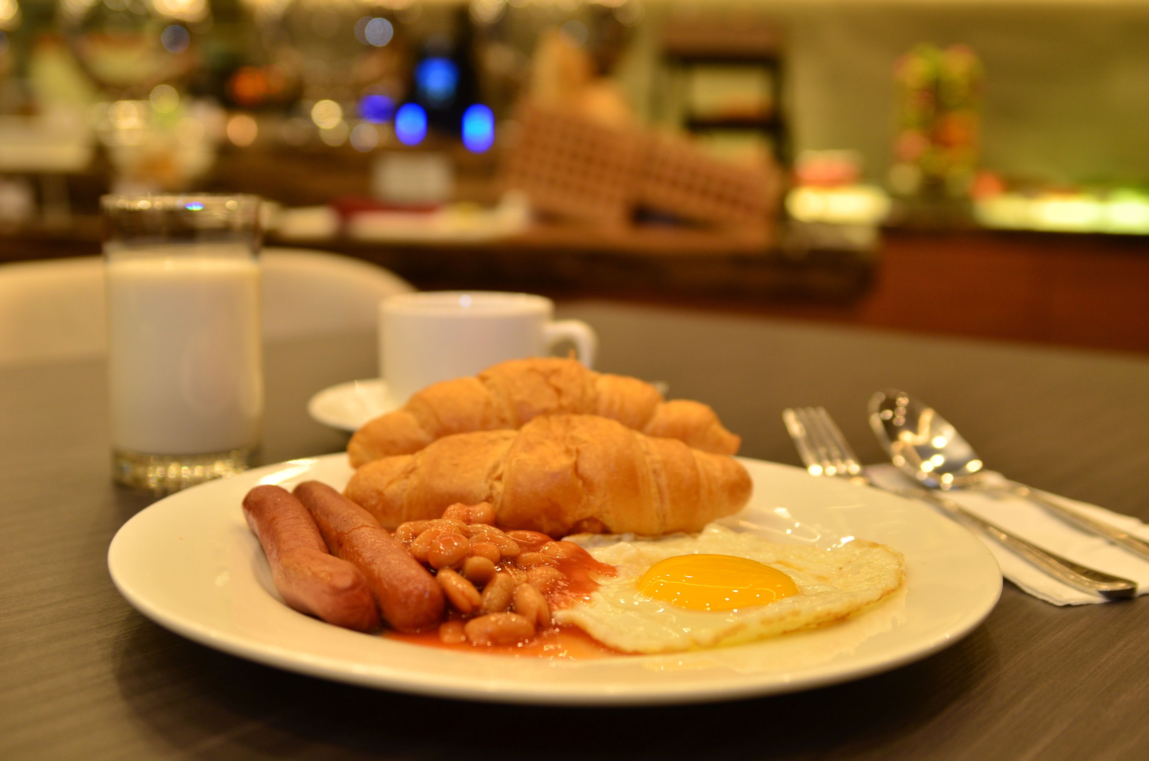Un plato de comida para el desayuno con huevos, salchichas, frijoles y croissants.