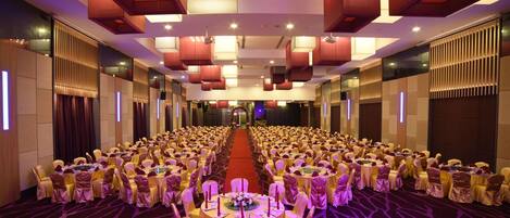 A banquet hall with round tables and chairs, a red carpet, and modern lighting fixtures.