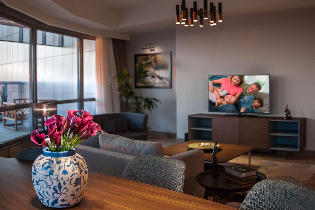 A modern living room with a sofa, a coffee table, and a TV. There is a vase with flowers on a table.