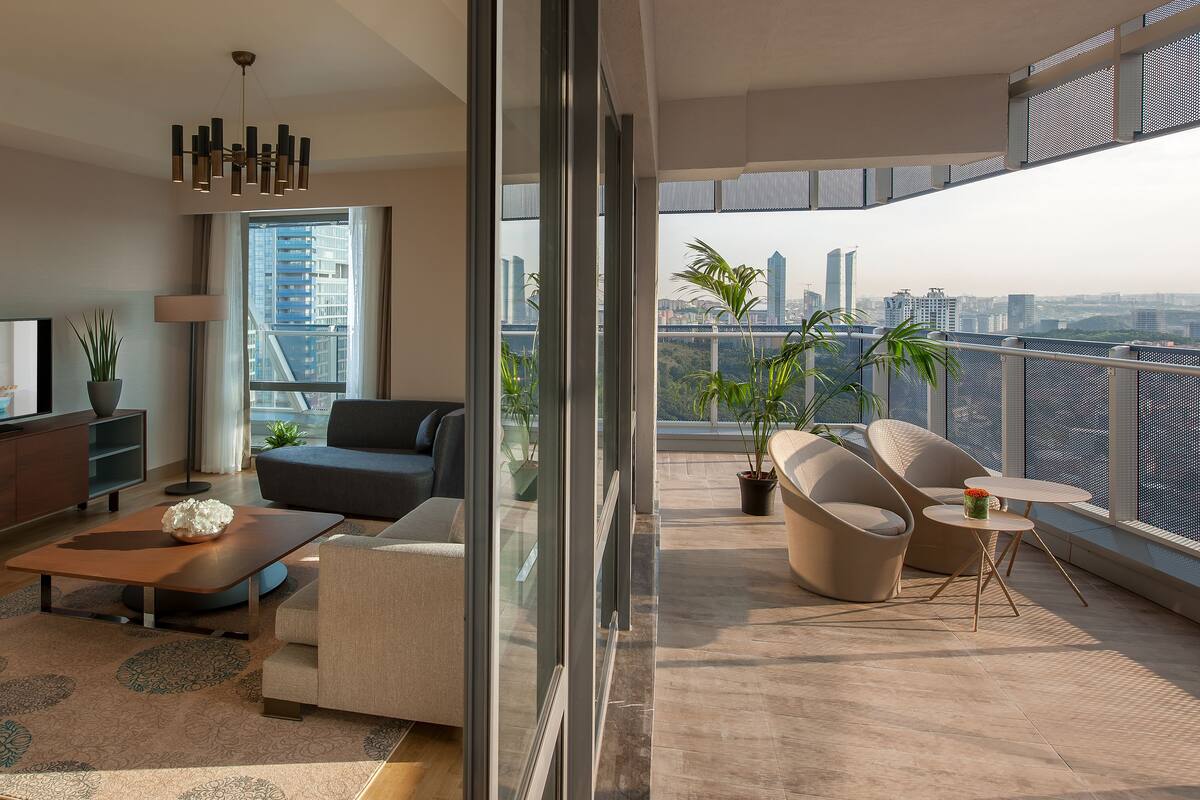 A modern living room with a large TV, sofa, coffee table, and balcony with city views.