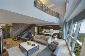 A spacious living area with a staircase leading to a balcony, a kitchen, and large windows offering a view of the landscape. - Somerset Maslak Istanbul (Sariyer)