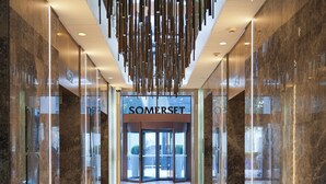Un moderno vestíbulo de hotel con piso de mármol pulido, una entrada central con puertas de vidrio y una lámpara colgante.