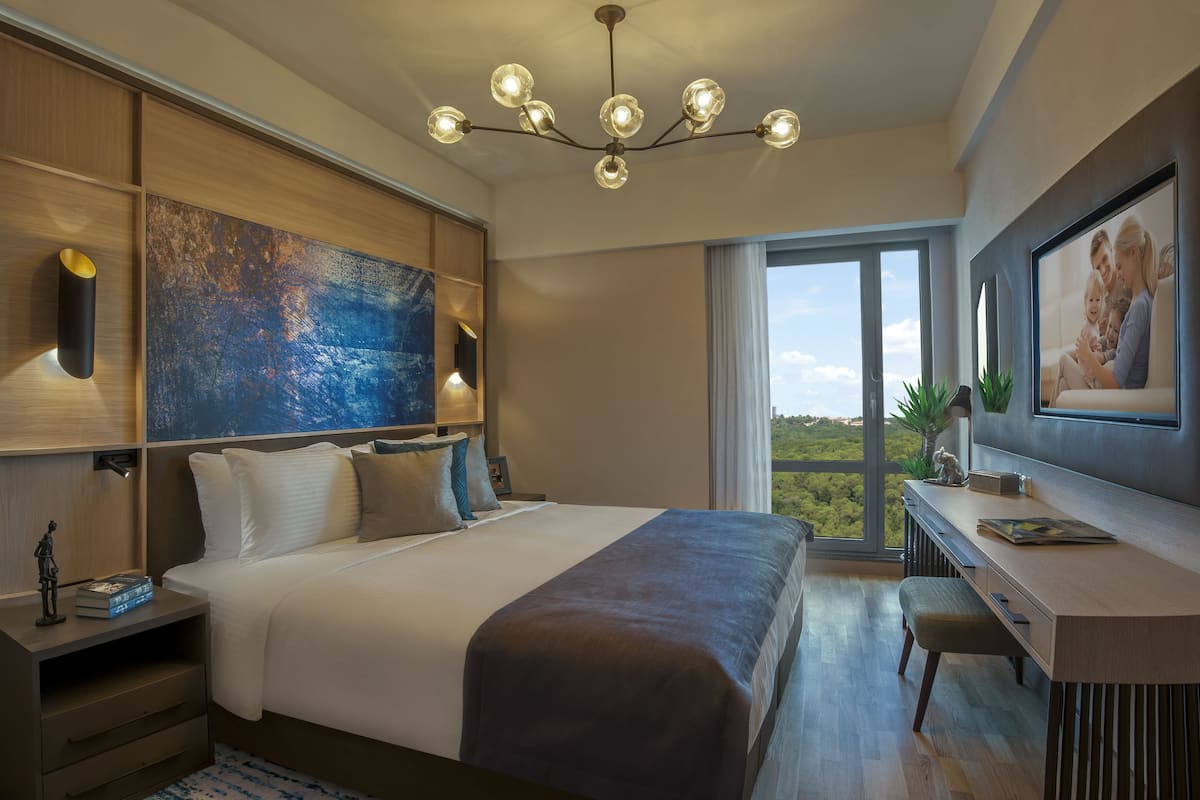 A modern hotel room with a large bed, a desk, and a view of the outdoors.