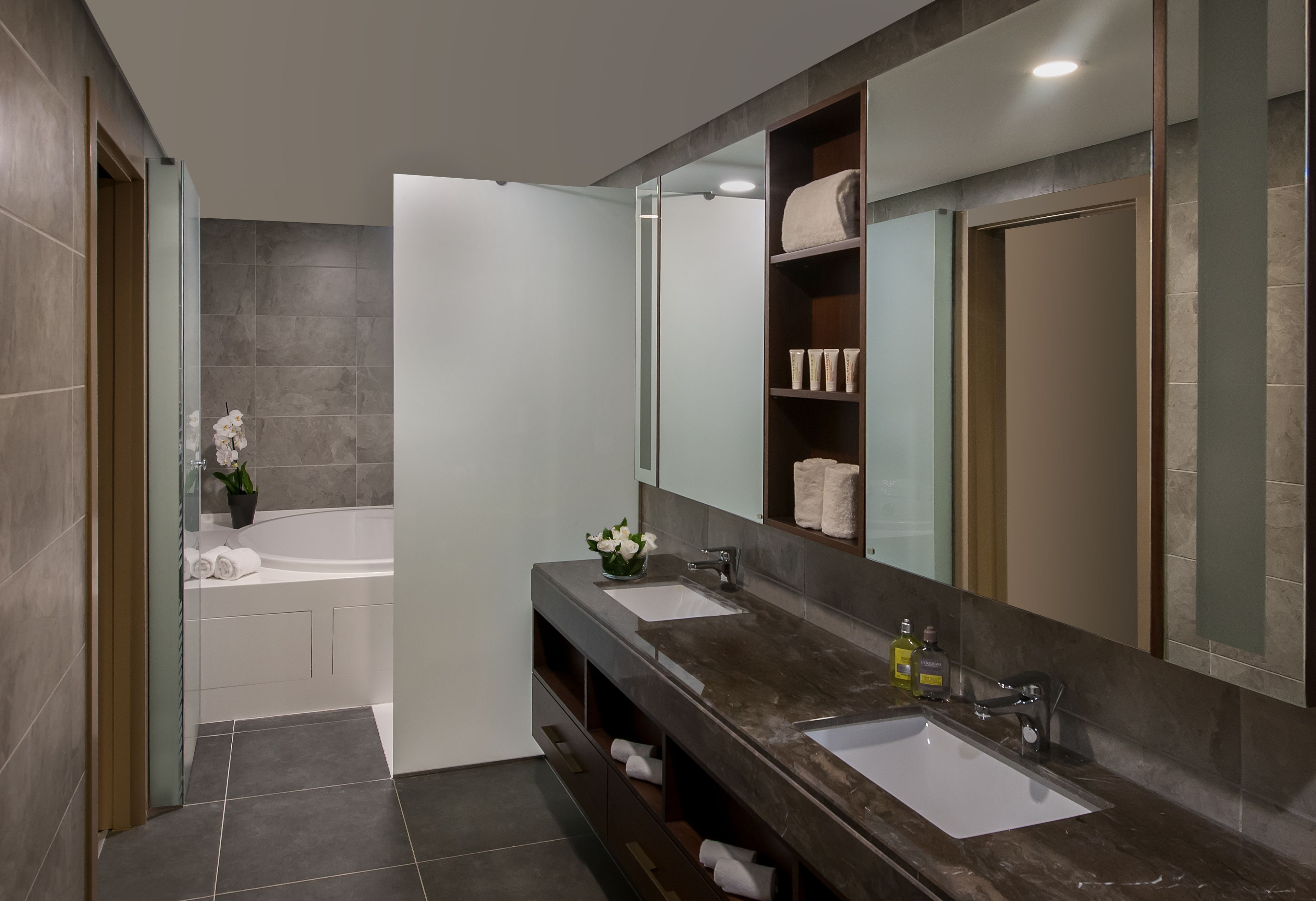 A modern bathroom with a bathtub, two sinks, a large mirror, and a vanity with shelves.