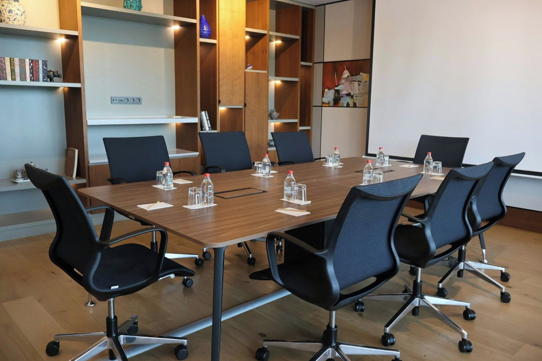 Un salón de conferencias con una larga mesa, seis sillas y botellas de agua sobre individuales.