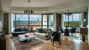A spacious living room with a large sofa, a coffee table, and a dining area with chairs. The room has large windows offering a view of the outdoors. - Somerset Maslak Istanbul (Sariyer)