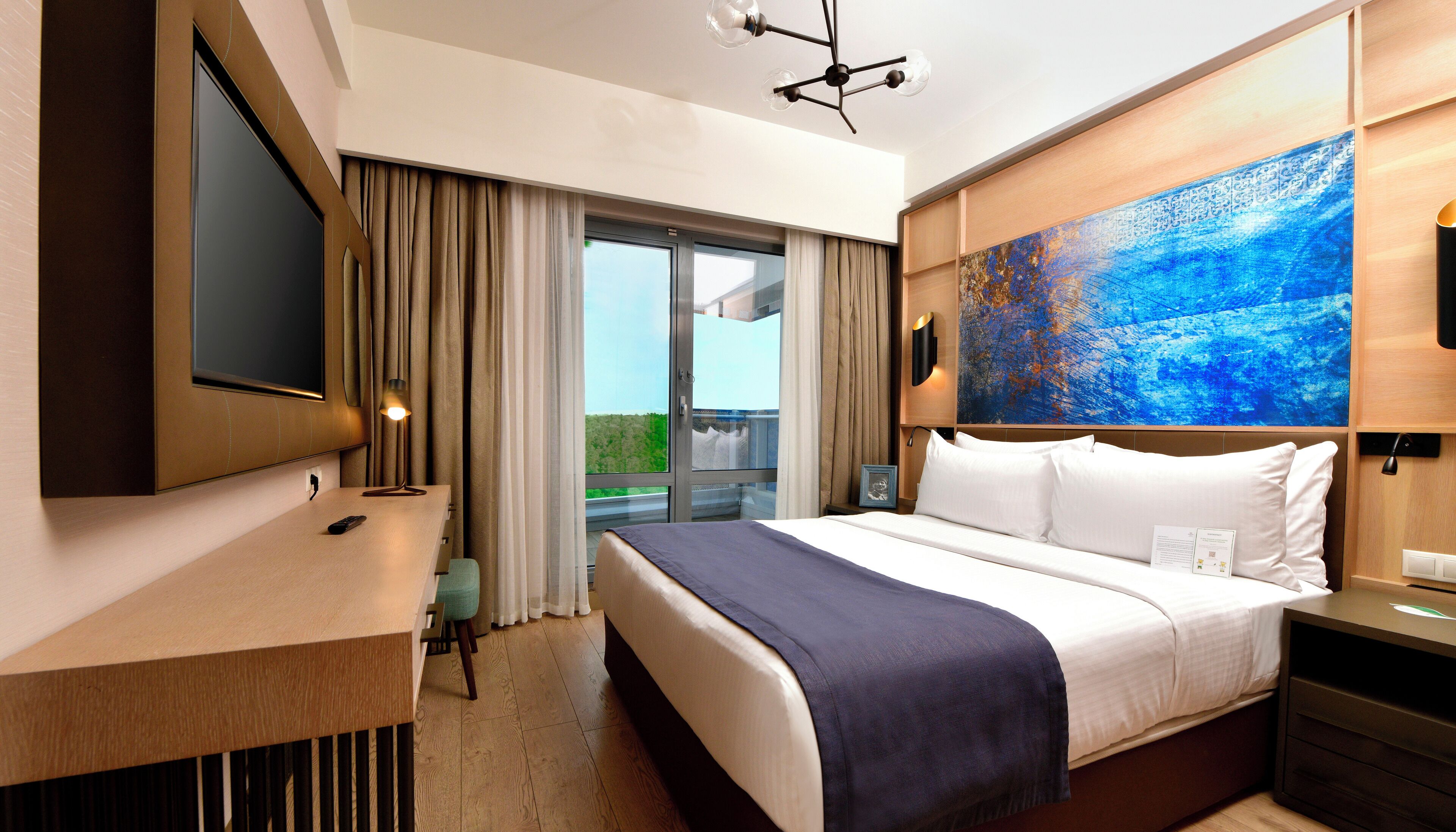 Une chambre d’hôtel avec un lit, une télévision, un bureau et un balcon avec des rideaux.