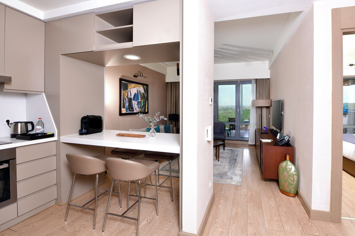 A modern hotel room with a kitchenette, a dining area, a living space, and a balcony with a view.