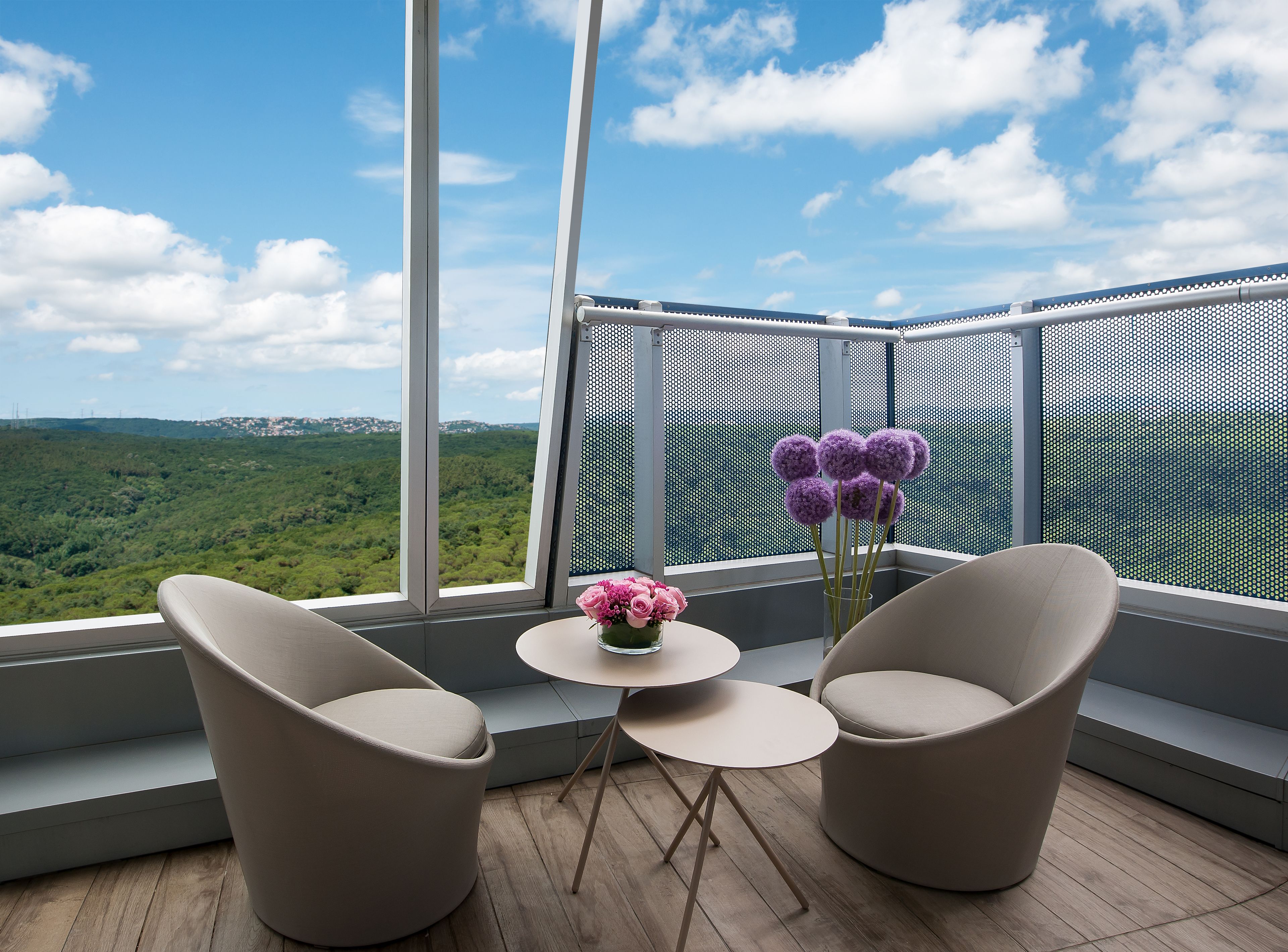 A balcony with two chairs, a small table, and a vase of flowers.