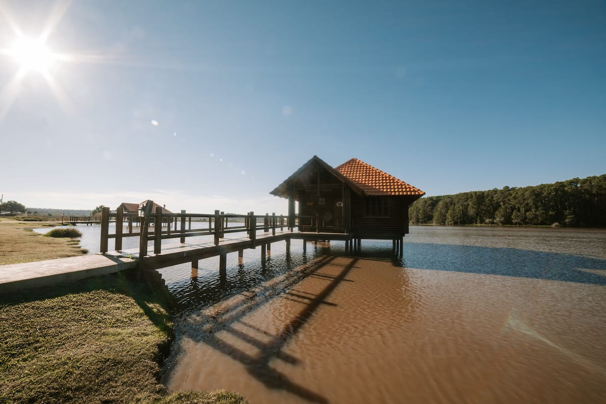 Une jetée en bois s’étendant au-dessus d’une étendue d’eau calme, menant à une petite cabane surmontée d’un toit en tuiles.