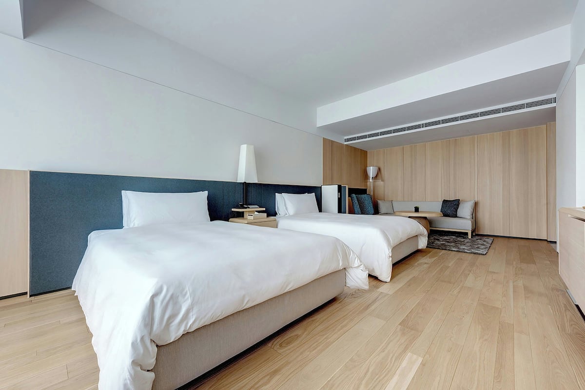 A modern hotel room with two beds, a desk, and a seating area.