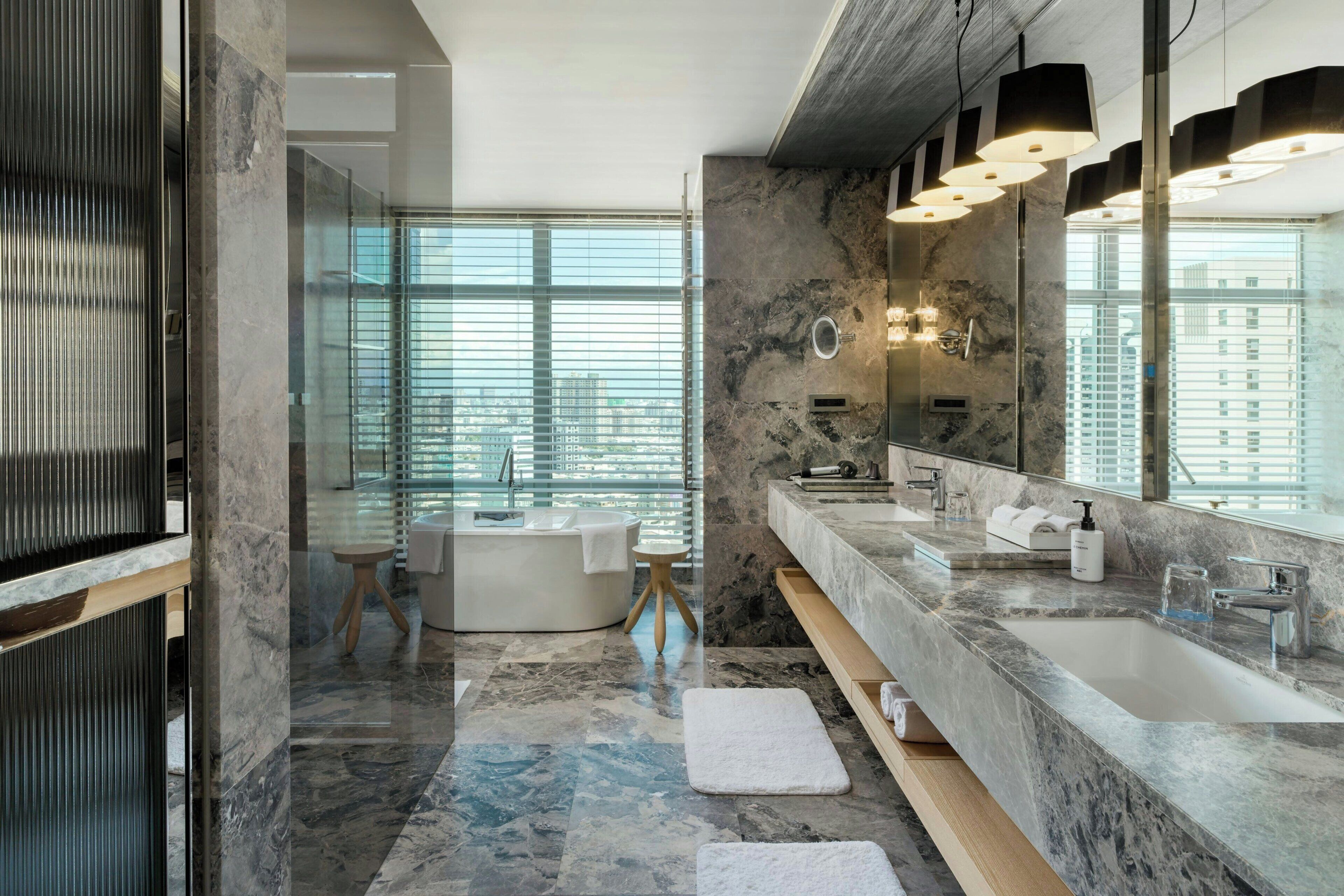 Un baño moderno con un espejo grande, encimeras de mármol y una bañera.