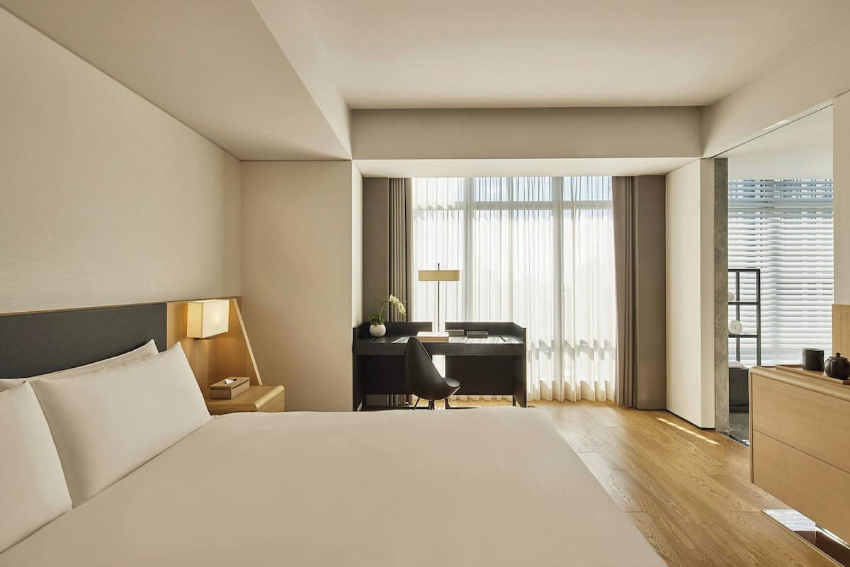 A hotel room with a large bed, a desk with a chair, a nightstand, and a dresser.