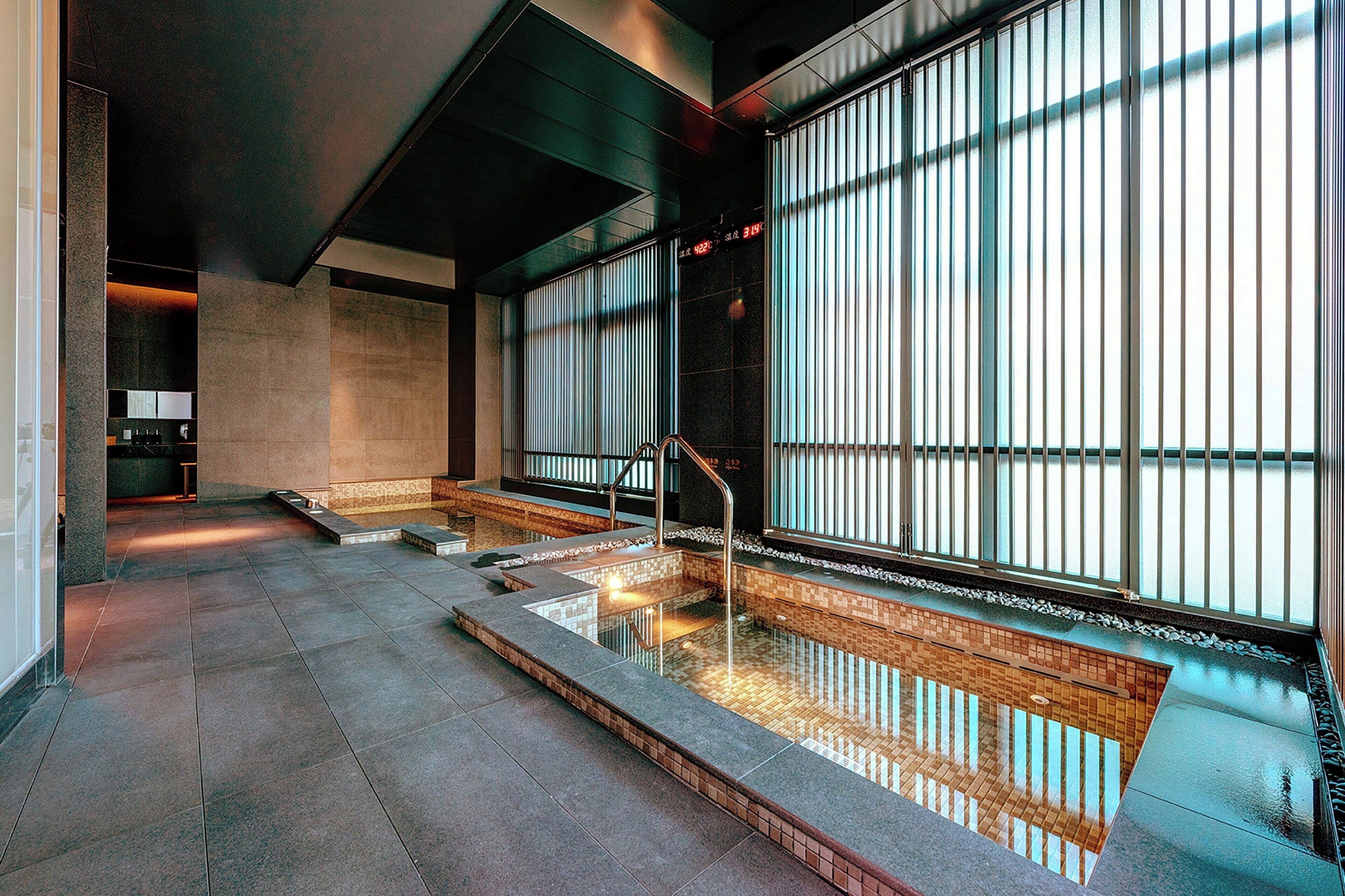 Un'area piscina interna moderna con pareti in vetro trasparente, pavimento piastrellato e ringhiera in metallo.