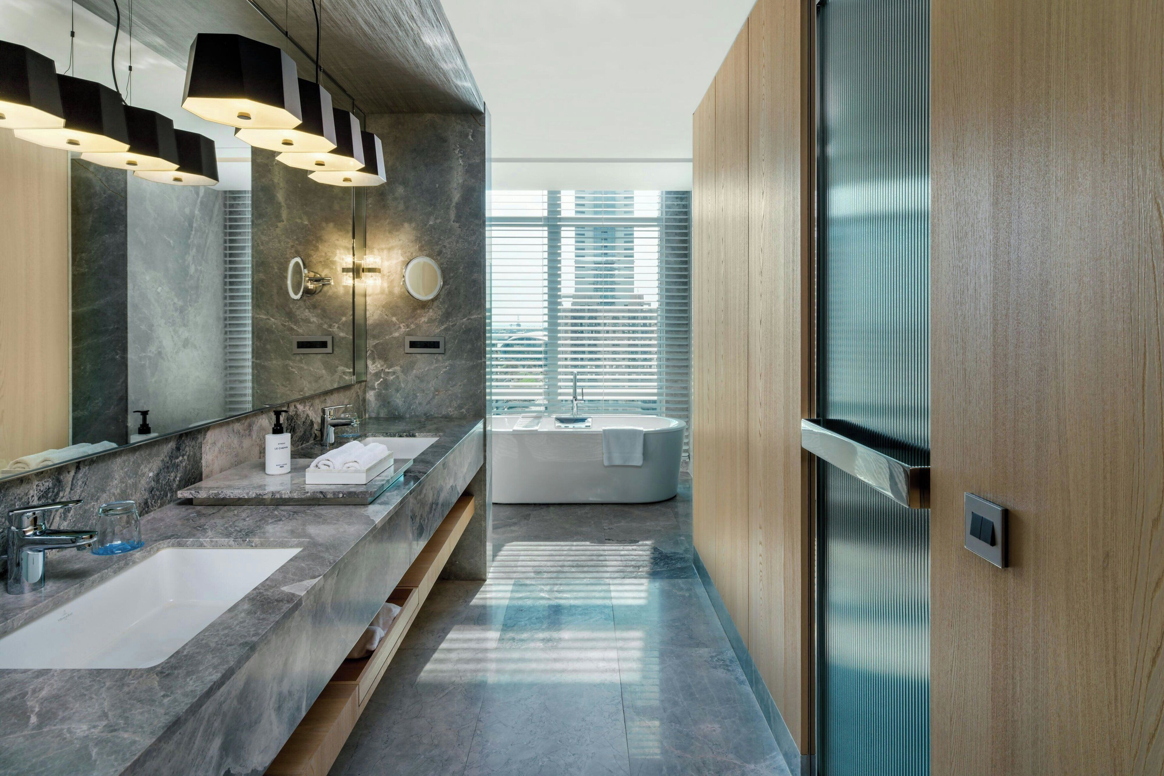 A modern bathroom with a large mirror, two sinks, a bathtub, and a wooden panel wall.