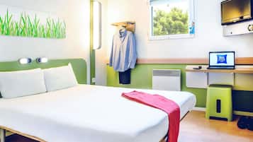 Habitación de hotel con cama, escritorio con una computadora portátil, ventana con vista a árboles y televisor montado en la pared.