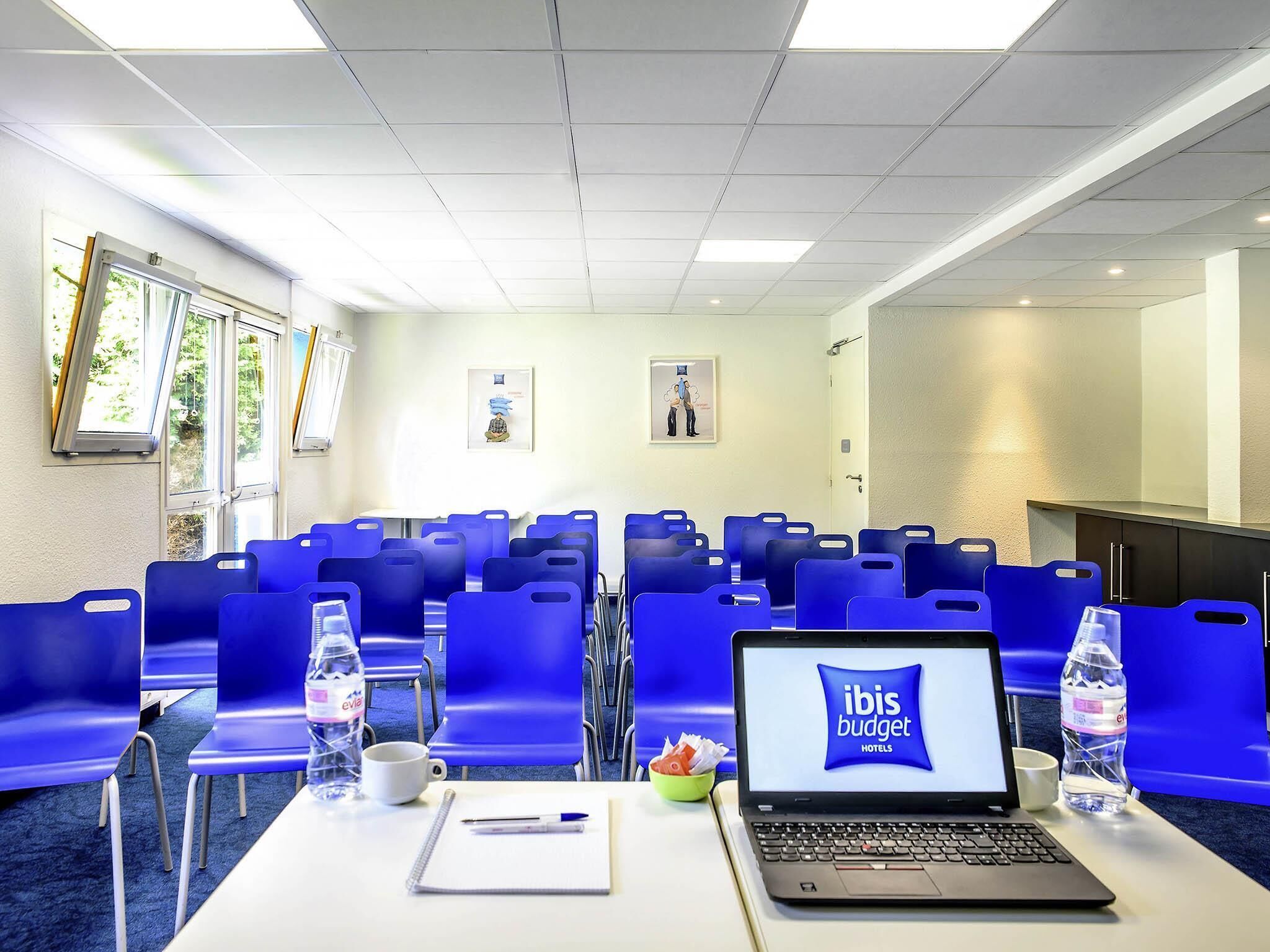 Una sala de conferencias con sillas azules, una computadora portátil, botellas de agua y una pizarra.
