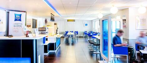 A modern hotel lobby with a reception desk, seating area, and a view of the dining section.