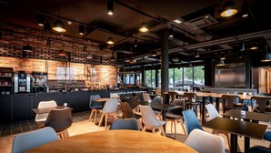 A modern cafe with brick walls, a bar area, and ample seating. - ibis budget Valenciennes Petite Forêt (Petite-Foret)