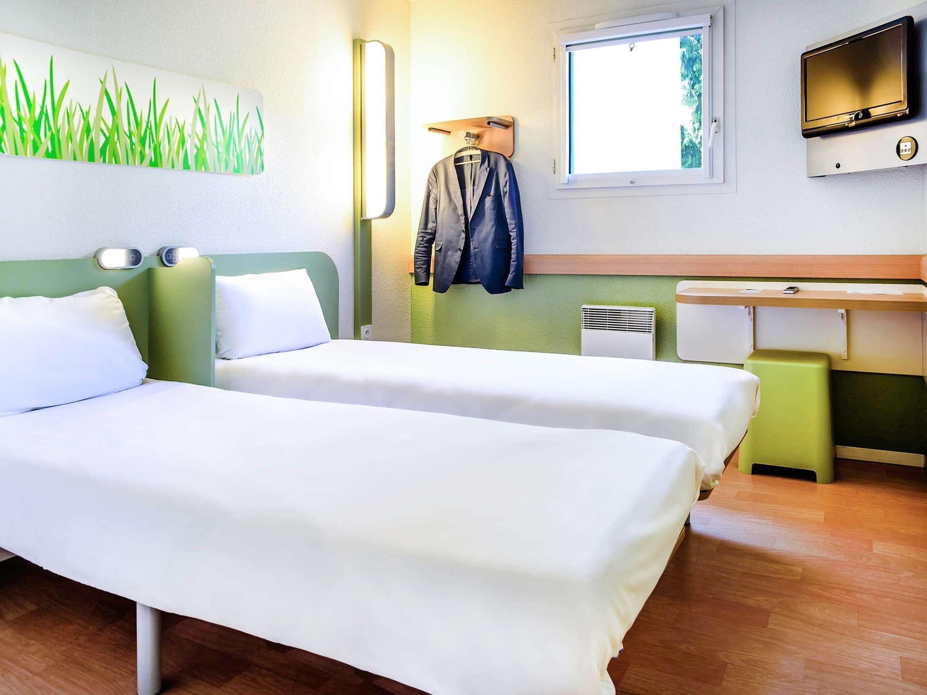 Ein Hotelzimmer mit zwei Betten, einem Schreibtisch, einem Fernseher und einem Fenster mit Blick.