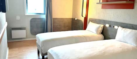 Una habitación de hotel con dos camas, una ventana con cortinas, una lámpara de pared y un calentador pequeño.