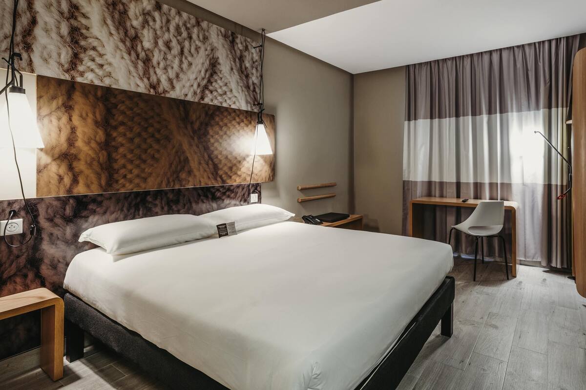 Habitación de hotel con una cama grande, un escritorio, una silla y un armario.