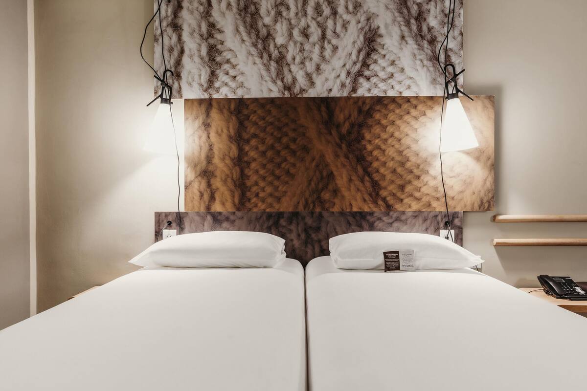 Habitación de hotel con una cama grande, cabecera de madera y mesita de noche con un teléfono.
