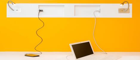 A white desk with a laptop and a smartphone connected to a wall-mounted charging station.