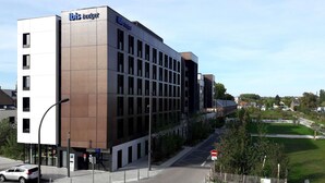 Um edifício moderno com a sinalização 'ibis budget', um estacionamento e uma placa de proibido acesso.